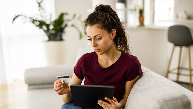 woman sat on sofa holding credit card and tablet