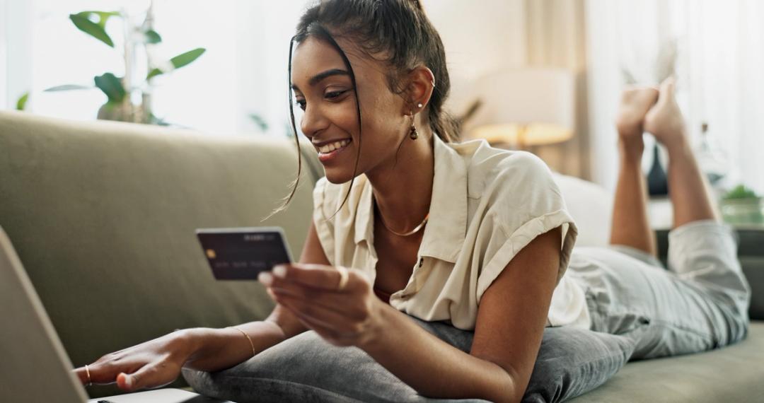 Woman on couch looking at her card in front of her laptop