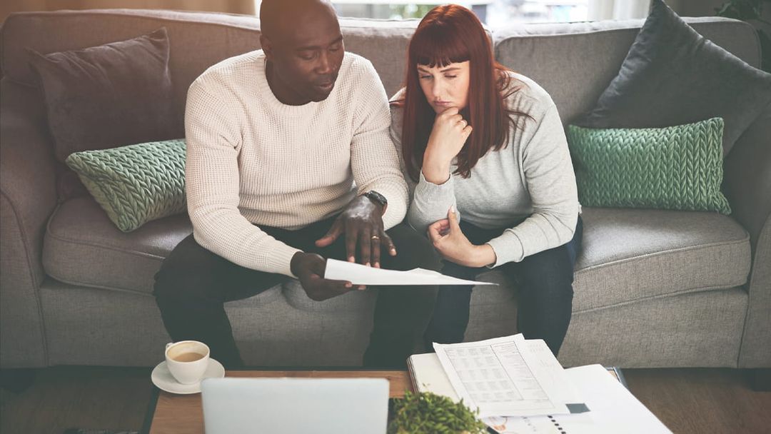 Couple sat on sofa in home setting reviewing paperwork together