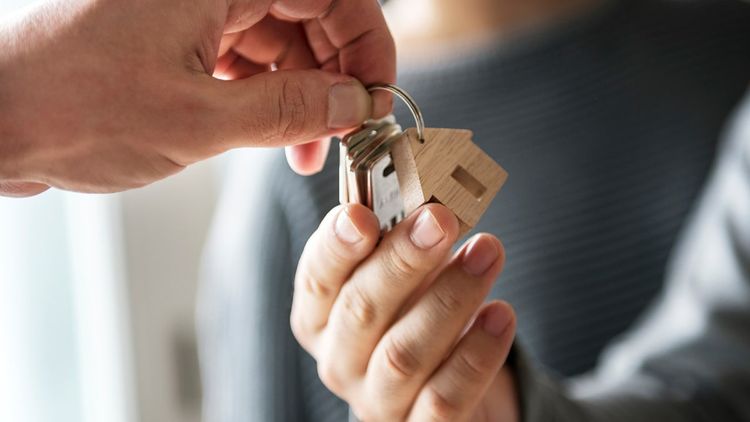 Close-up of an estate agent's hand passing keys to another adult person's hand