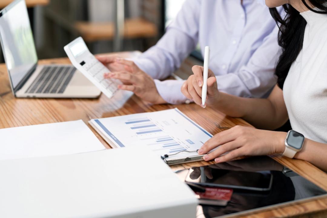 Two people looking at a calculator and a laptop