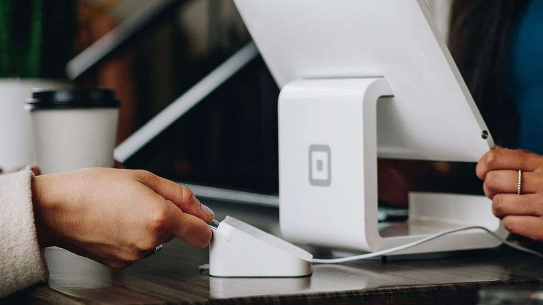 Close-up of one adult person working on a till with human hand inserting chip and pin via card reader.