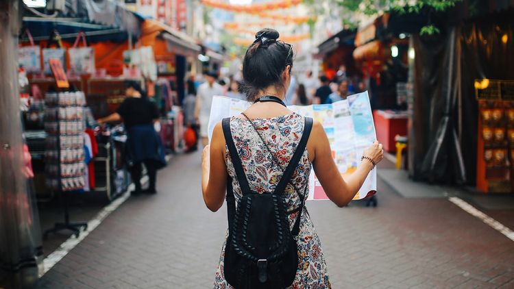 Young adult woman enjoying exploring a foreign market with map in hand.