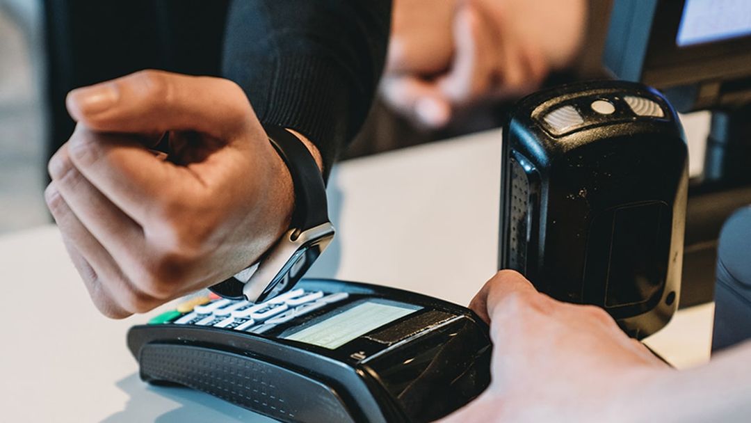 Close-up of an adult man using smart watch to pay at a contactless credit card reader.