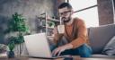 Man drinking coffee sitting on sofa using laptop in home setting