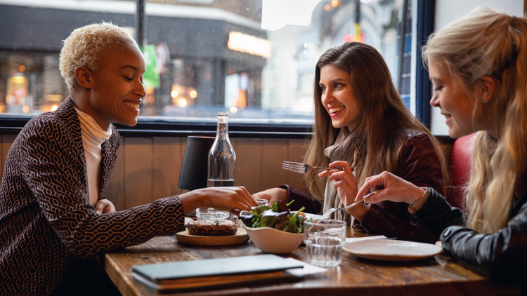 Three female adult friends socialising over a meal in a restaurant setting