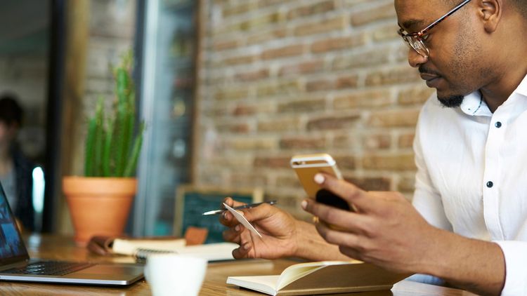 A single adult male businessman working indoors with mobile phone and credit card in hand.