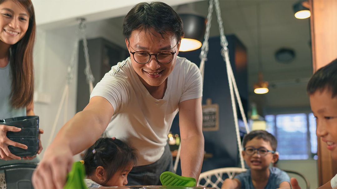 Smiling family sitting down to dinner with young children, getting settled at the table.