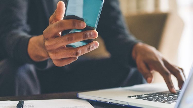 Close-up of adult man working on laptop with wireless technology and mobile phone.