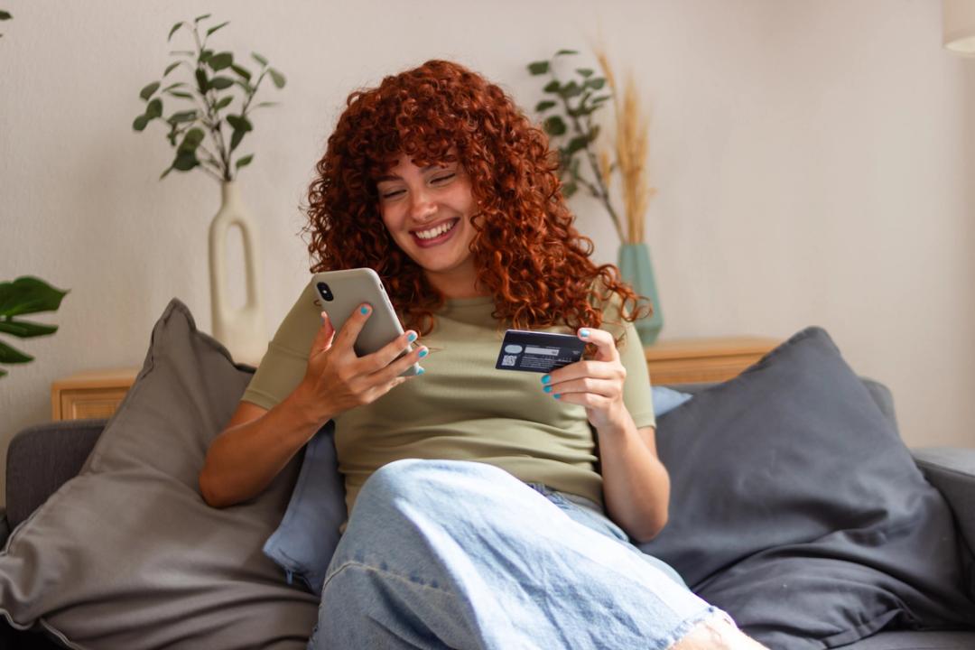 Girl smiling checking her phone and holding her credit card