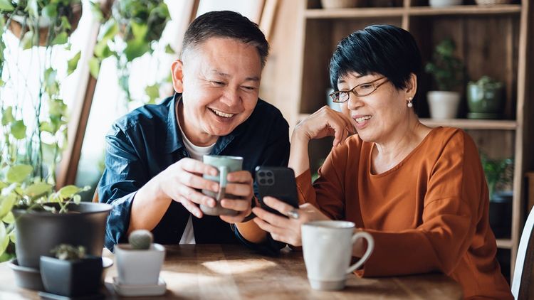 One adult male and one adult female sitting in a café holding coffee mug and looking at phone screen together