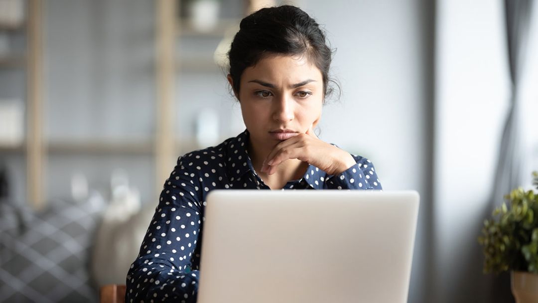 Woman looks pensively at laptop in a home setting