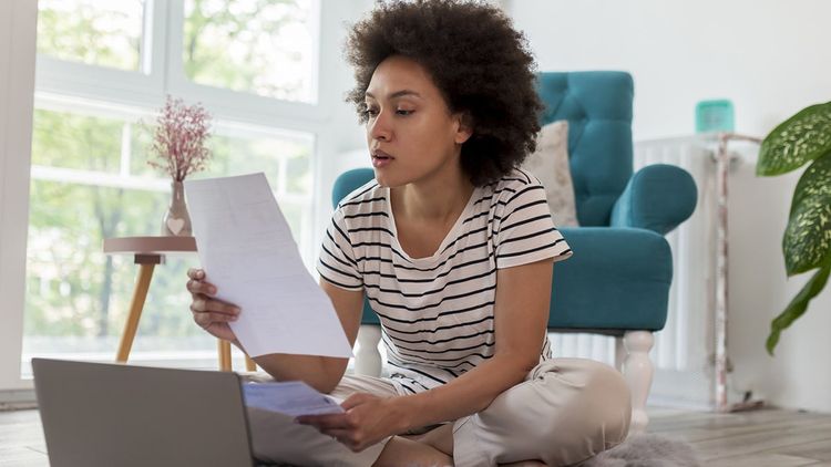 Indoors, one adult female sitting and working in home interior, wearing casual clothing and reviewing paperwork.