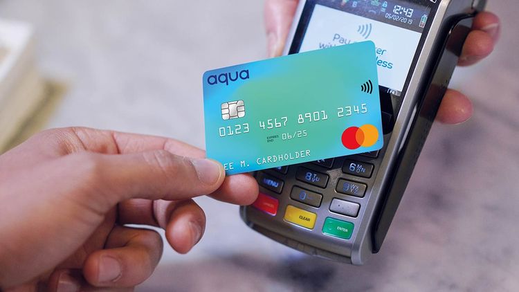 Close-up of human hand holding credit card over contactless credit card reader to pay for shopping.