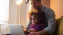 Indoor living room setting: man sitting with child on lap working on a laptop