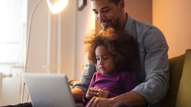 Indoor living room setting: man sitting with child on lap working on a laptop