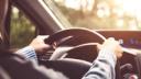 One person driving a car, hands on the steering wheel, with sunlit background