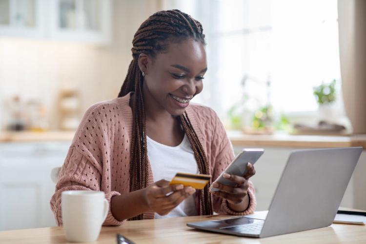 Woman looking at her phone and card in front of a laptop