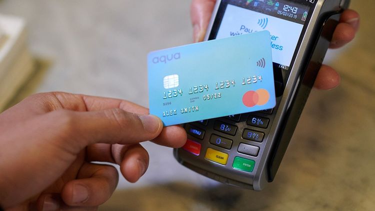 Close-up of human hand holding credit card over contactless credit card reader to pay for shopping
