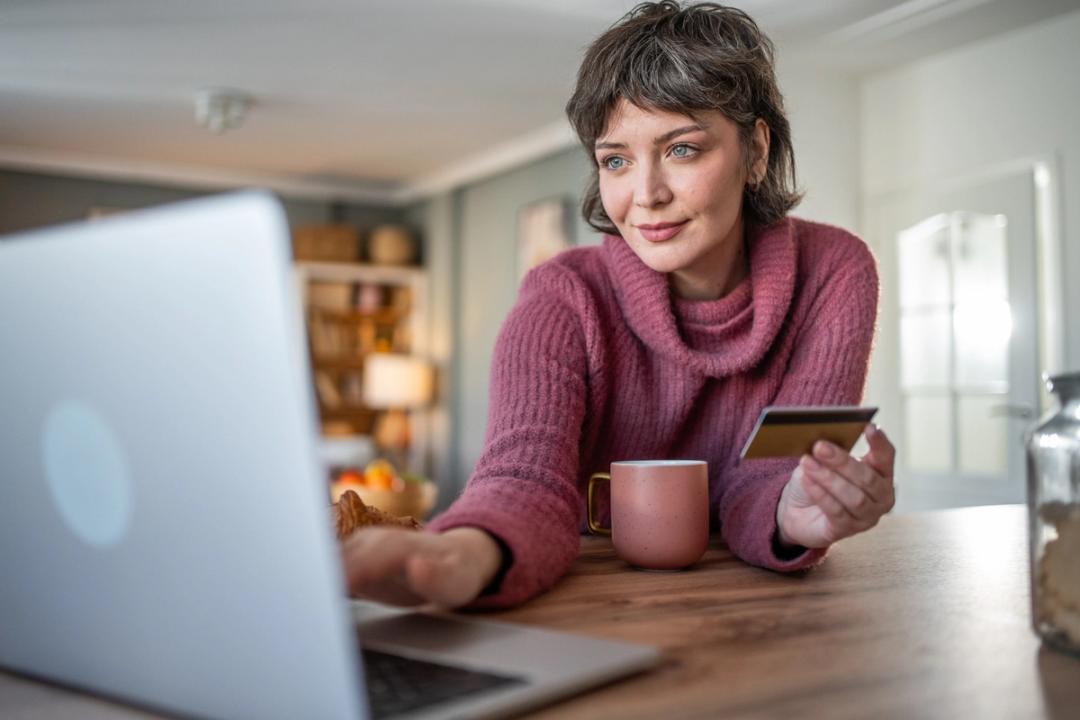 Women in pink jumper looking at her laptop while holding a credit card