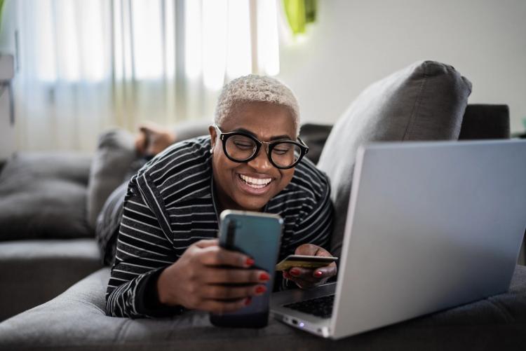 Woman smiling at her phone, holding her credit card in front of a laptop