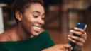 Young adult smiling woman, looking at smart phone, reflecting positivity and happiness.
