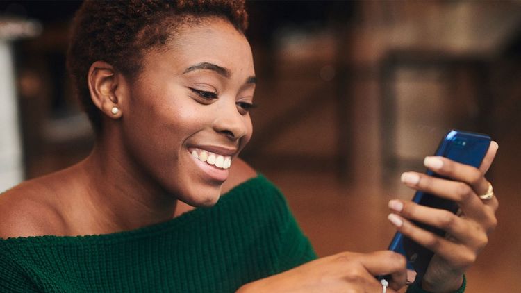 Young adult smiling woman, looking at smart phone, reflecting positivity and happiness.