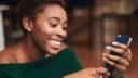 Young adult smiling woman, looking at smart phone, reflecting positivity and happiness.