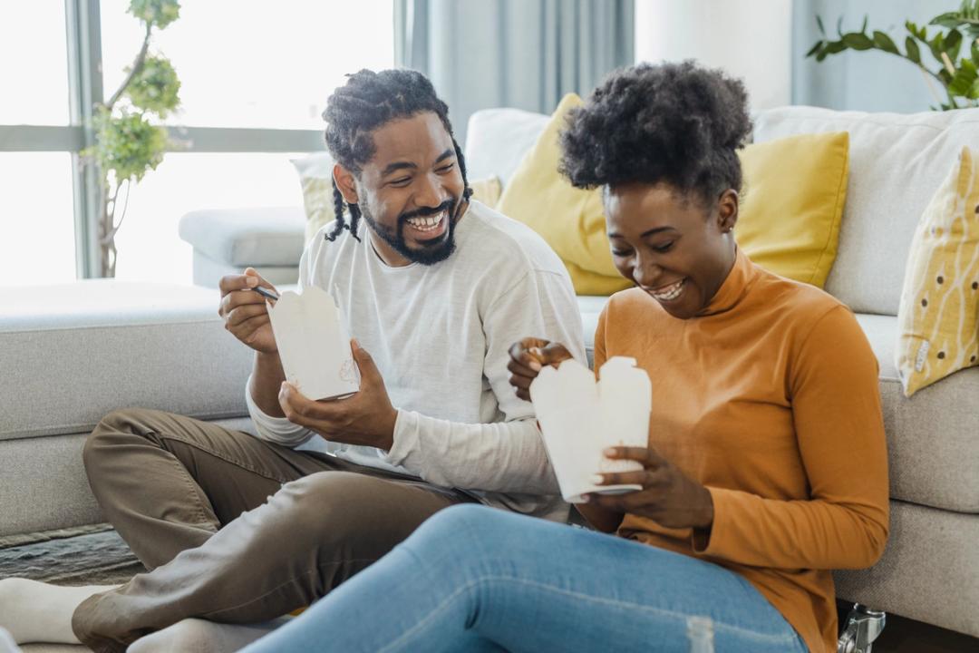 Couple holding takeaway boxes while sat on the floor
