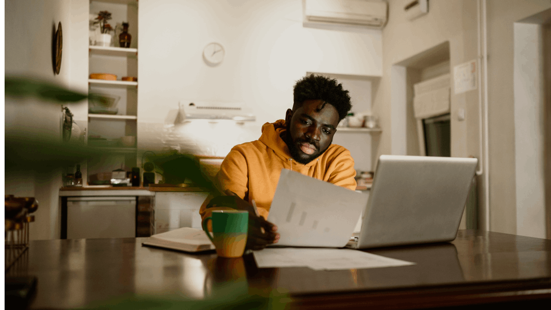 Man looking at paperwork whilst sat at table with laptop