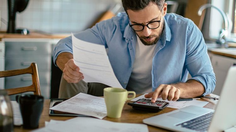 One adult male sitting indoors working with calculator and laptop