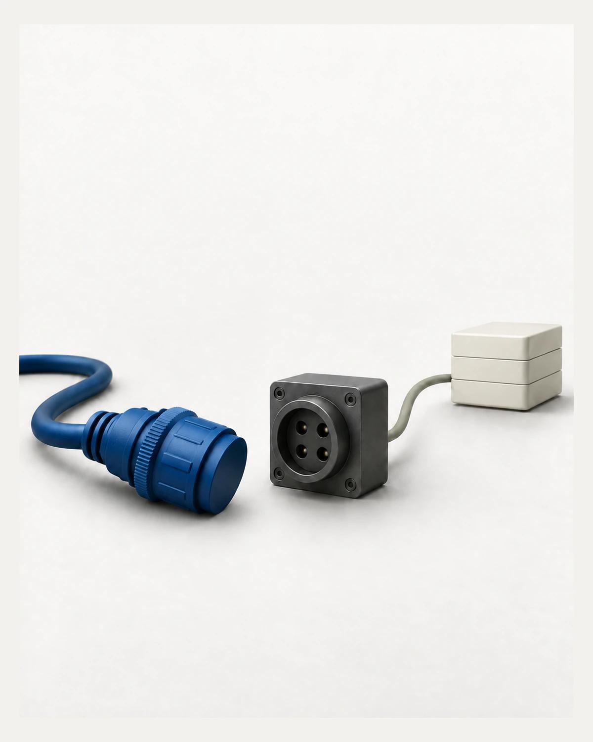 A capped cobalt connector lies disconnected beside a graphite socket, with a grey cable leading to three stacked ivory modules.
