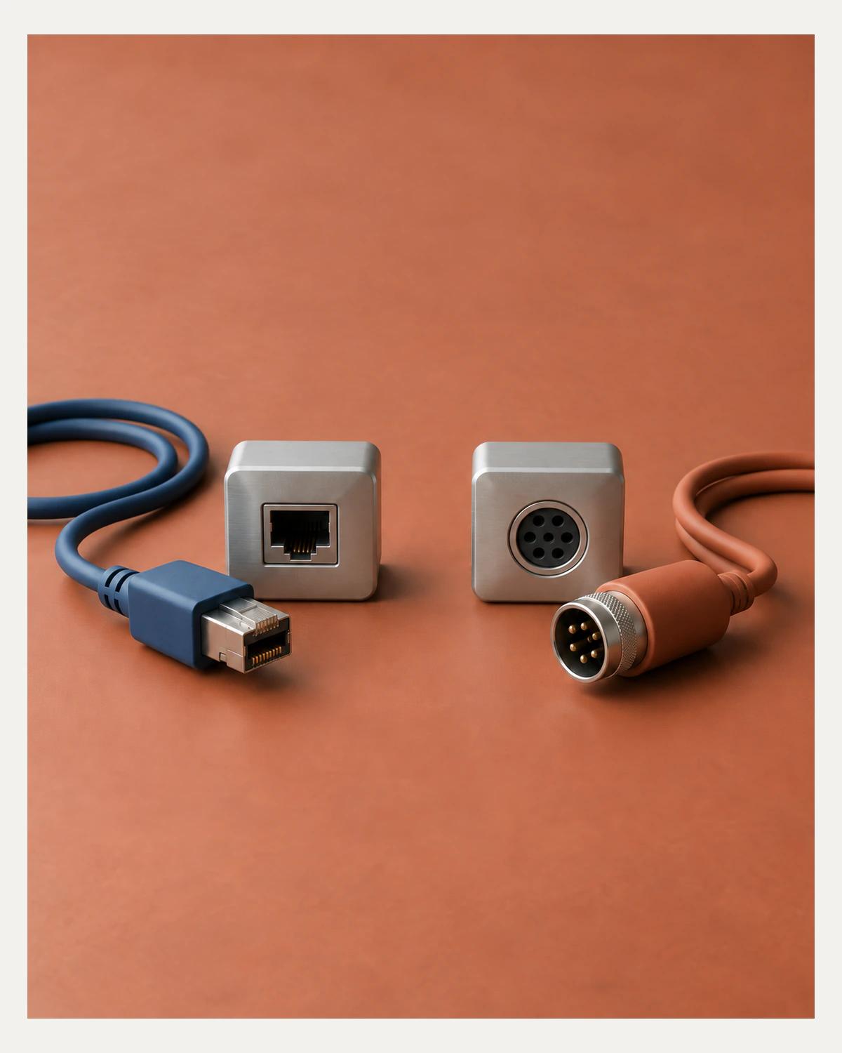 Blue rectangular and orange round connector plugs lie beside separate matching metal sockets on a terracotta surface.
