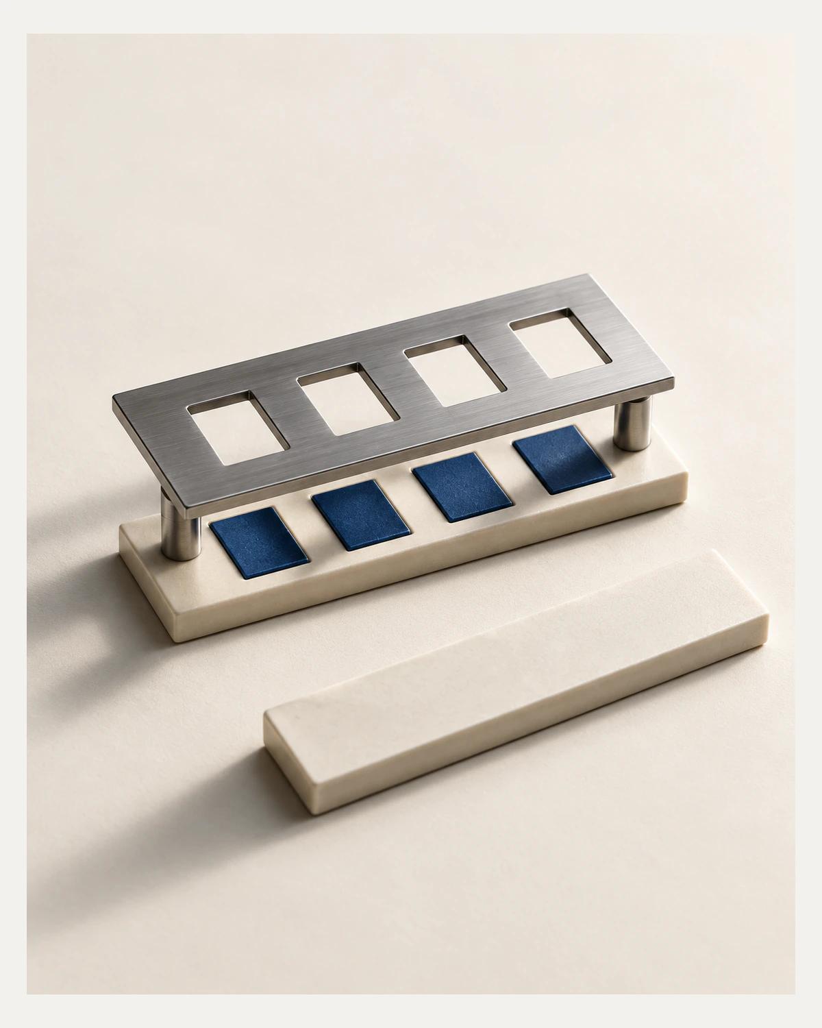 A raised steel stencil with four apertures stands over an ivory strip with four blue inserts, beside a blank ivory strip.