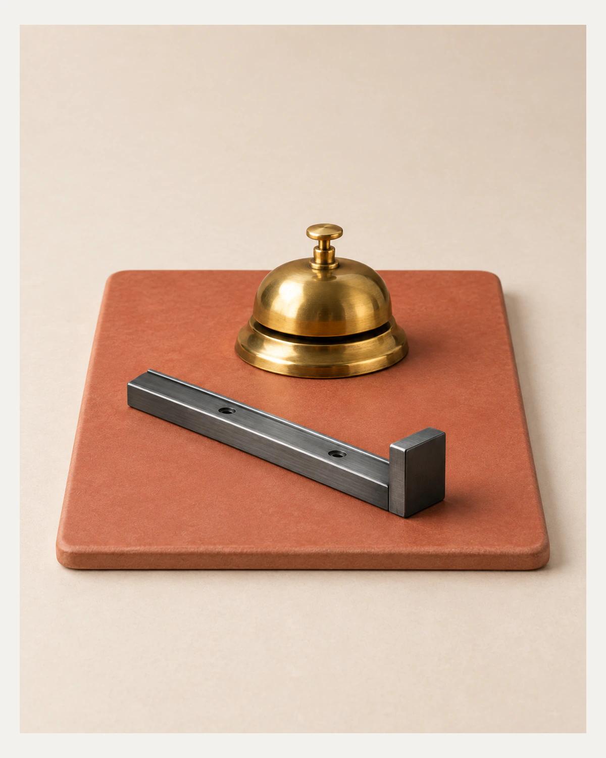 A brass service bell and a graphite rail with a raised end stop rest on a terracotta tile on a pale desk.