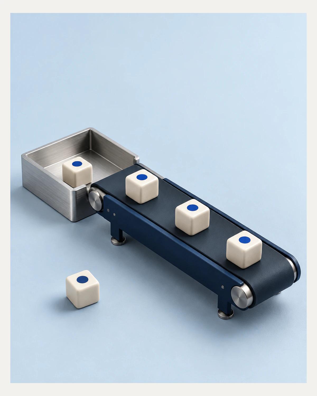 A navy miniature conveyor carries ivory cubes marked with cobalt dots towards a metal tray; another cube rests beside the belt.