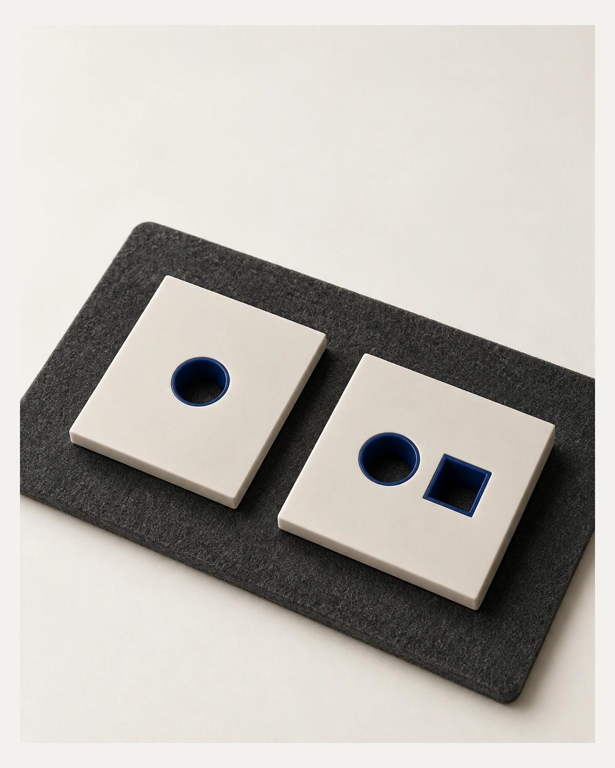 Two ivory plates rest on charcoal felt; both have cobalt-lined round openings and the right plate also has a square opening.