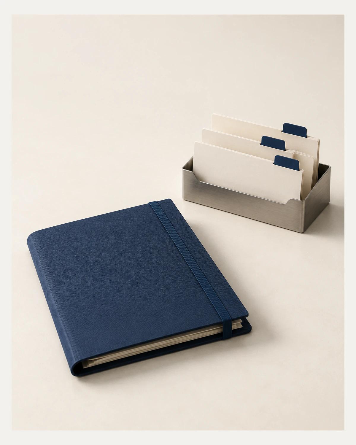 A navy cloth document folio lies apart from three ivory tabbed cards in a brushed-metal rack on an ivory desk.