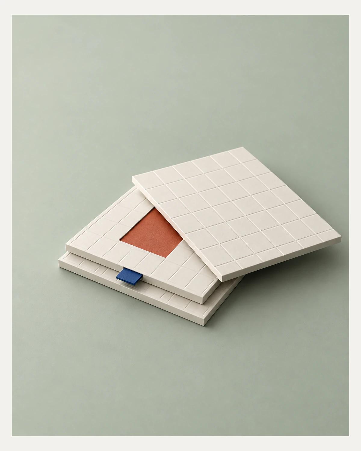 Offset ivory grid panels expose a terracotta square beneath the top layer, with a cobalt tab on a pale sage surface.