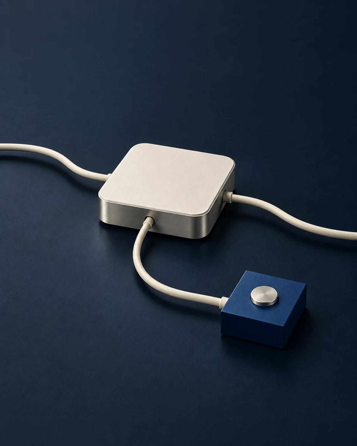 A brushed metal network appliance connected by cream cables to a small cobalt checkpoint on an ink-blue table.