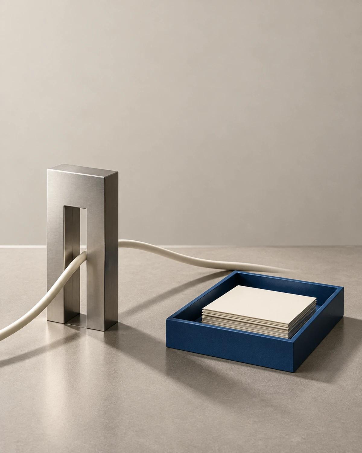 A cream cable passing through a tall metal gate beside a cobalt tray of blank cards on warm grey stone.