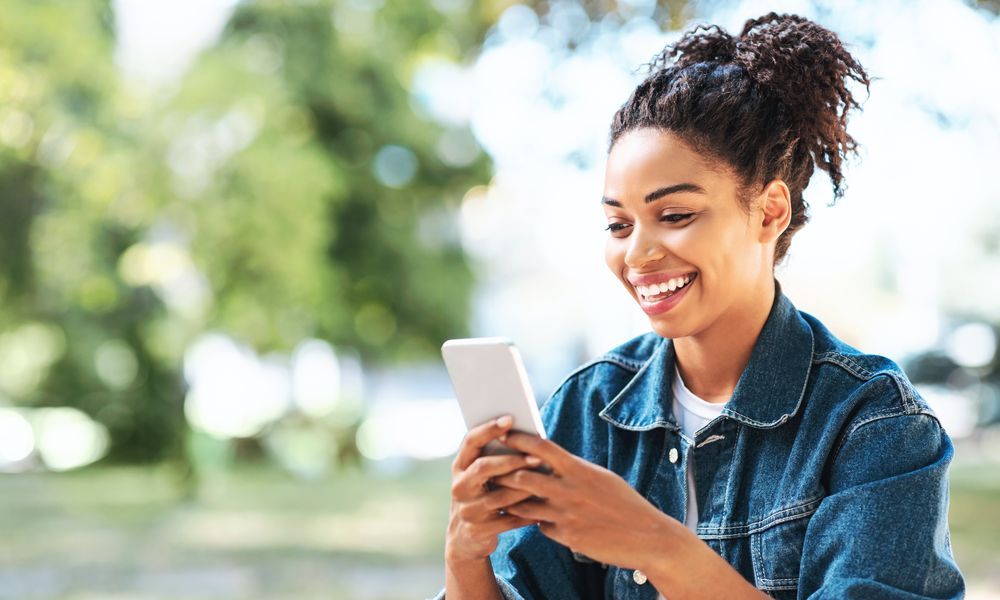 Smilende dama med en mobil i hånden som hun ser på