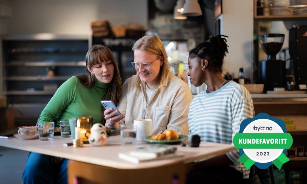 Tre venner sitter ved et bord og ser på en mobil