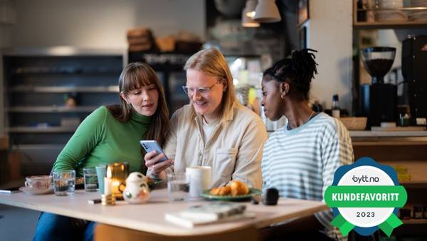 Tre venner sitter ved et bord og ser på en mobil