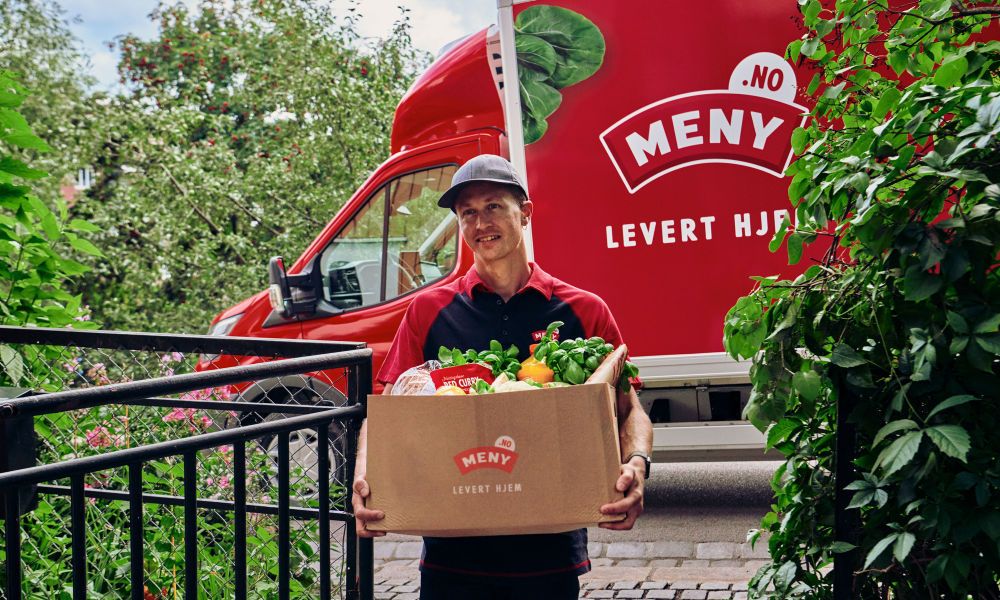 Smilende MENY ansatt leverer varer fra MENY helt hjem til kunde