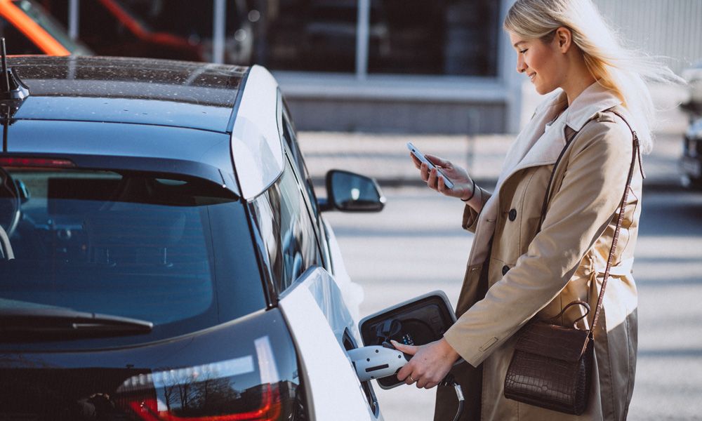 En dame setter inn eller tar ut ladekabel på en el-bil