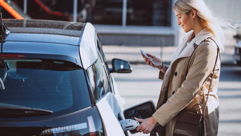 En dame setter inn eller tar ut ladekabel på en el-bil