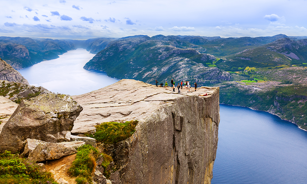Utsikt over Preikestolen med mennesker som står på fjellplatået og fjorden i bakgrunnen.