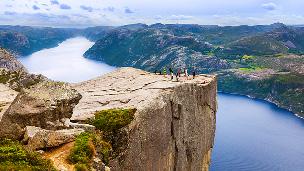 Utsikt over Preikestolen med mennesker som står på fjellplatået og fjorden i bakgrunnen.