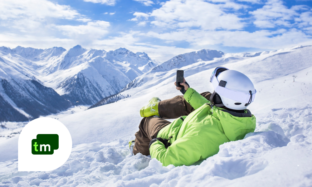 Et menneske ligger i snøen og holder en telefon foran seg